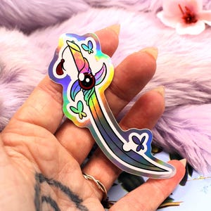 May include: A holographic sticker of a rainbow-colored sword with a single eye and butterfly details.