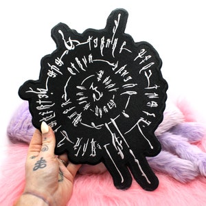 Może przedstawiać: Czarna naszywka haftowana z białymi literami w okrągłym wzorze. Litery są w stylizowanym kroju pisma i zawierają słowa "The" i "Truth".