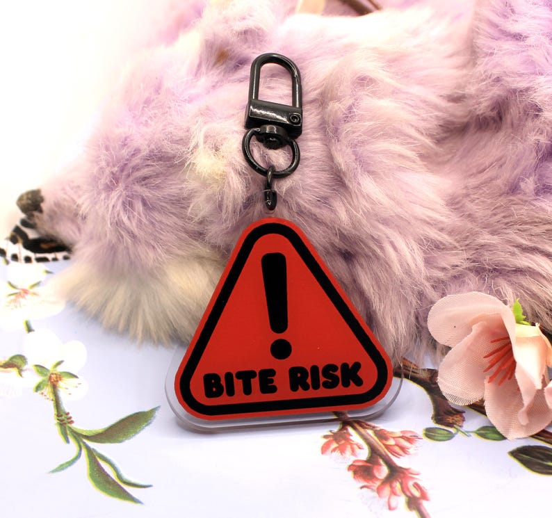 This 5cm triangluar acrylic charm is the perfect addition to any keyring or ita bag! The design features a triangluar red warning sign with the text '! BITE RISK' in large letters. It is double sided with a lobster clasp for easy fastening.