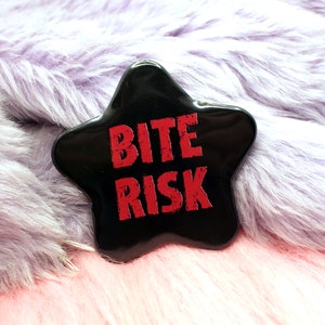 Könnte beinhalten: Ein schwarzer sternförmiger Pin mit der Aufschrift "Bite Risk" in roten Buchstaben.