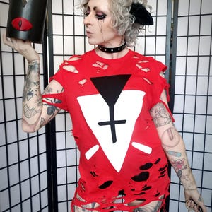 May include: A red distressed t-shirt with a white and black graphic design. The person is holding a black crown with a red eye design. The person is wearing a black choker and striped socks.