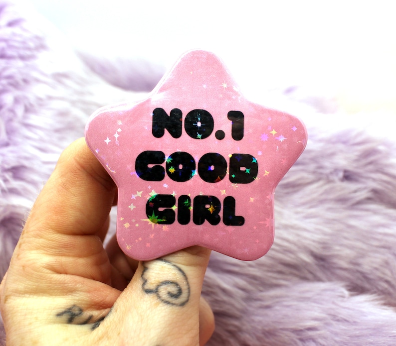 Puede incluir: Bot&oacute;n rosa en forma de estrella con purpurina y el texto "No.1 Good Girl" en negro.