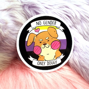 Può includere: Un adesivo rotondo con sfondo nero e bordo bianco. L'adesivo presenta un cane di cartone animato con guance rosa e una striscia gialla, bianca e viola dietro di lui. Il testo "NO GENDER ONLY DOGGY" è scritto su uno striscione bianco.