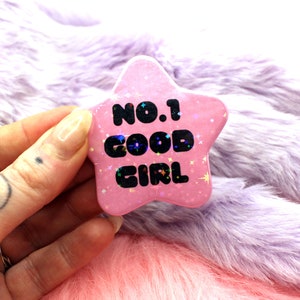 Puede incluir: Pin de estrella rosa con purpurina y el texto "NO.1 GOOD GIRL" en negro.