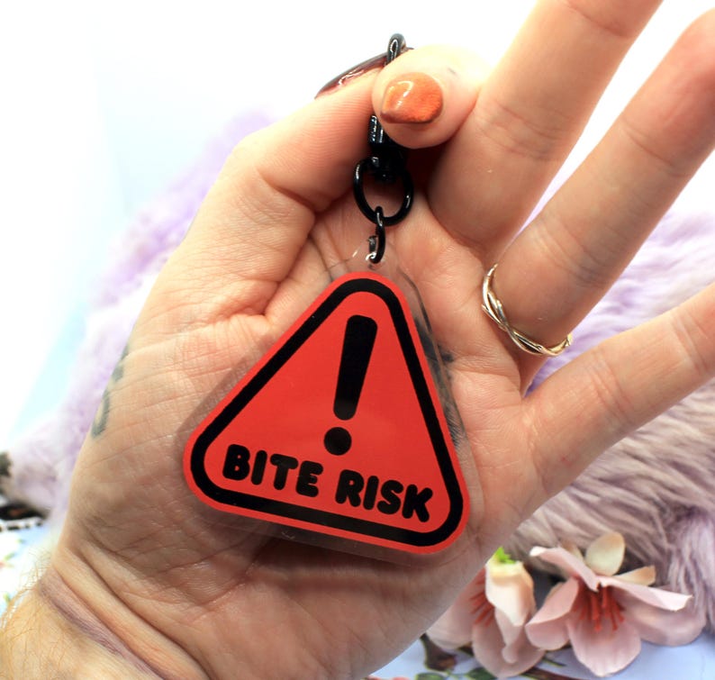 This 5cm triangluar acrylic charm is the perfect addition to any keyring or ita bag! The design features a triangluar red warning sign with the text '! BITE RISK' in large letters. It is double sided with a lobster clasp for easy fastening.