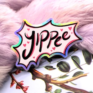 May include: A pink and iridescent sticker with the word "YIPPEE" in black lettering and pink hearts.