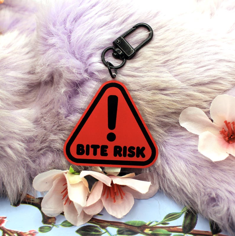 This 5cm triangluar acrylic charm is the perfect addition to any keyring or ita bag! The design features a triangluar red warning sign with the text '! BITE RISK' in large letters. It is double sided with a lobster clasp for easy fastening.