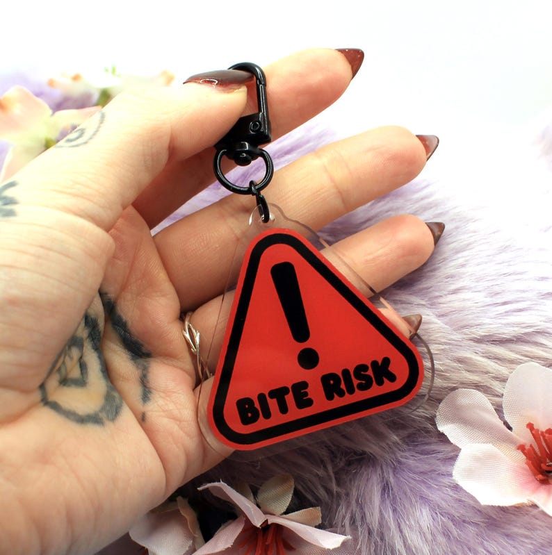 This 5cm triangluar acrylic charm is the perfect addition to any keyring or ita bag! The design features a triangluar red warning sign with the text '! BITE RISK' in large letters. It is double sided with a lobster clasp for easy fastening.
