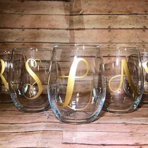 May include: Set of six clear glass wine glasses with gold lettering. Each glass has a different letter, R, S, L, A, and S.