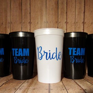 Puede incluir: Seis vasos de pl&aacute;stico con exteriores negros y blancos. Los vasos tienen texto azul que dice "Team Bride". Un vaso es blanco con texto azul que dice "Bride".