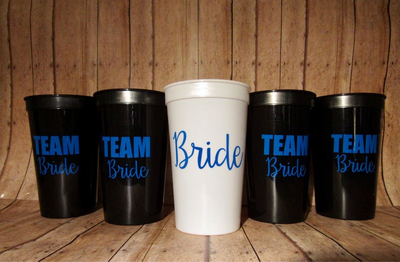 Puede incluir: Seis vasos de pl&aacute;stico con exteriores negros y blancos. Los vasos tienen texto azul que dice "Team Bride". Un vaso es blanco con texto azul que dice "Bride".