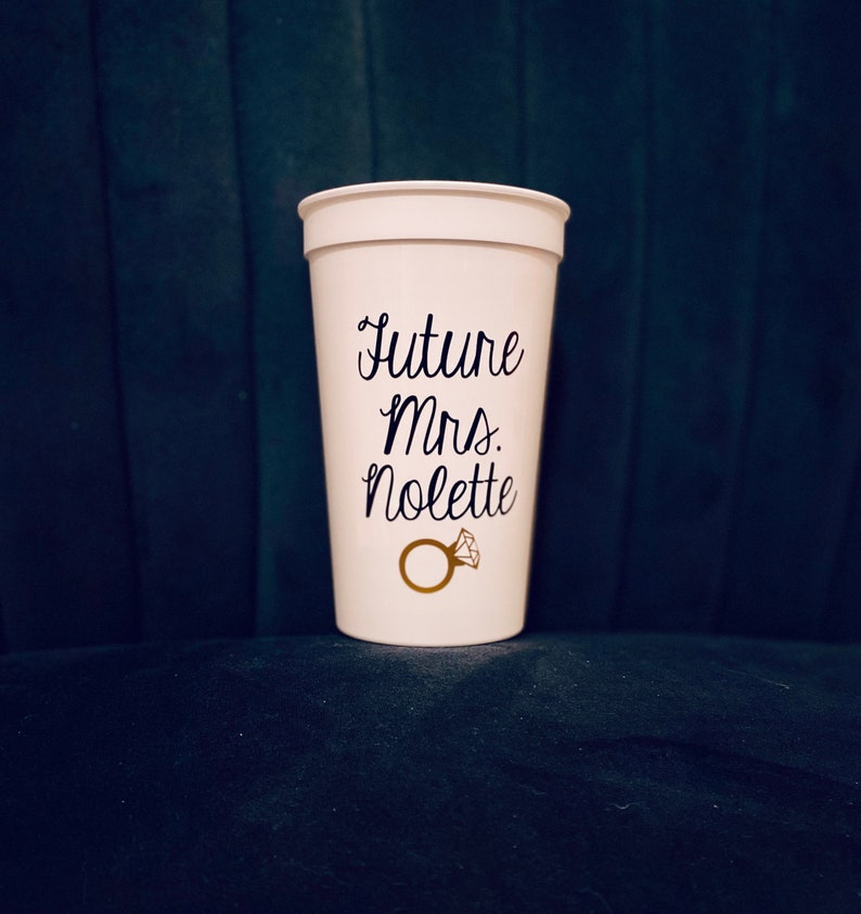 May include: White plastic cup with the text "Future Mrs. Nolette" and a gold ring with a diamond on it.