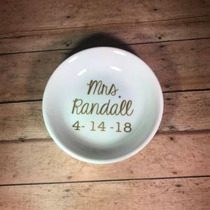 May include: White ceramic ring dish with gold lettering that reads "Mrs. Randall 4-14-18".