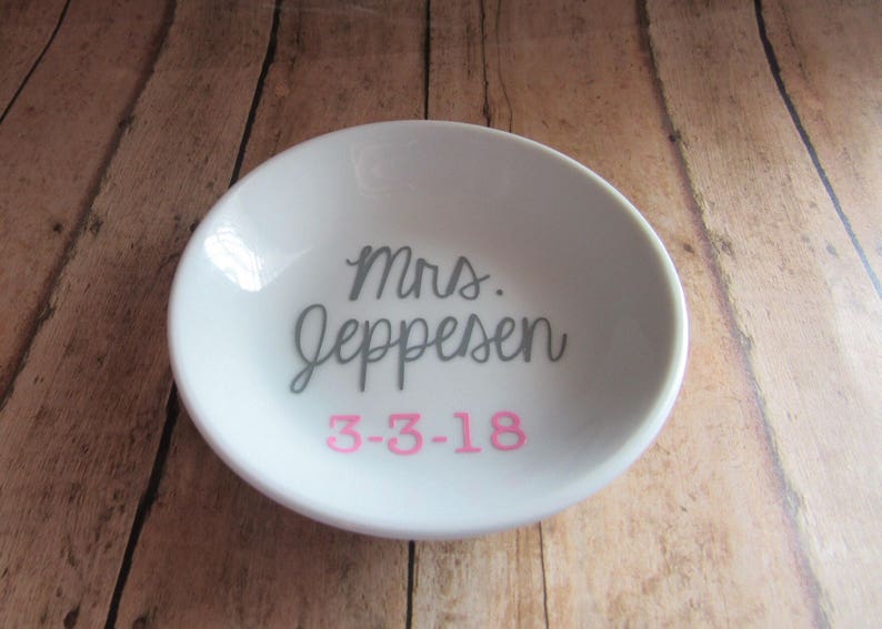 May include: White ceramic ring dish with the text "Mrs. Jeppesen" in gray and "3-3-18" in pink.