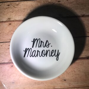 May include: White ceramic ring dish with black lettering that reads "Mrs. Maroney".