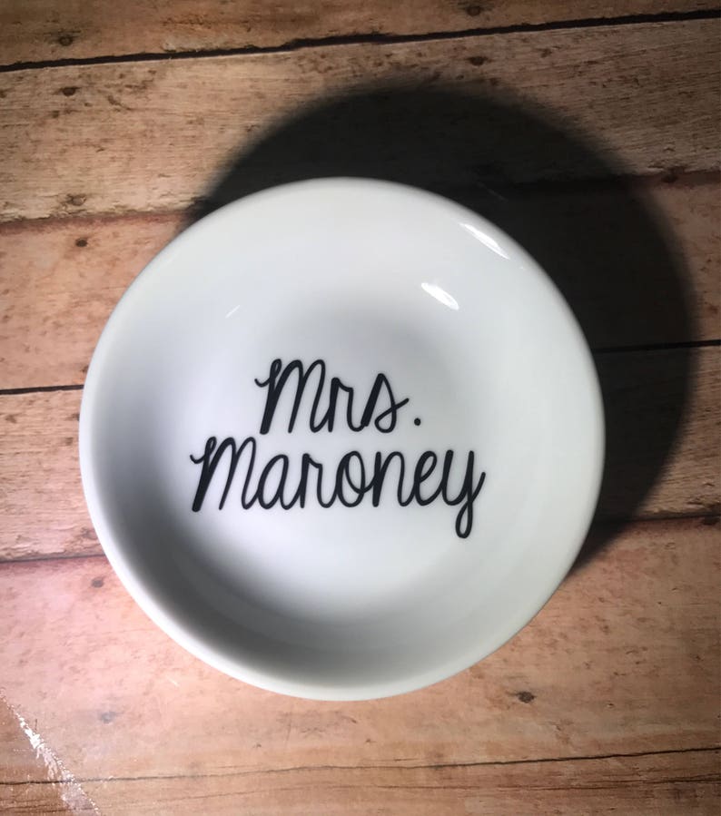 May include: White ceramic ring dish with black lettering that reads "Mrs. Maroney".