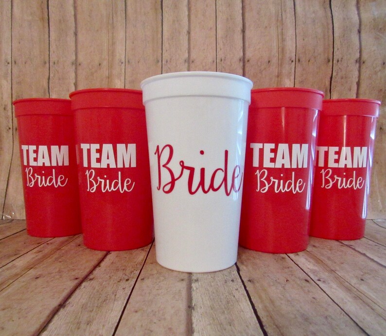 Puede incluir: Cinco vasos de pl&aacute;stico rojos con letras blancas que dicen "Team Bride" y un vaso de pl&aacute;stico blanco con letras blancas que dicen "Bride".