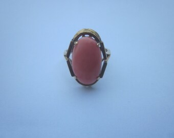 May include: A gold ring with a pink oval-shaped gemstone set in a geometric design.