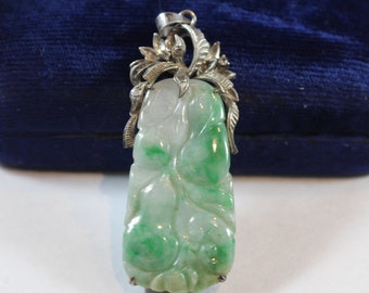 May include: A green jade pendant with intricate silver floral detailing. The jade is carved with a leafy design and has a white and green color.