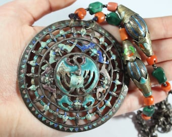 May include: A silver and enamel pendant necklace with a circular design featuring a bird and floral motifs. The pendant is surrounded by a beaded chain with coral and green stones.