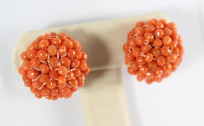 May include: A pair of orange coral earrings, each earring is a sphere made of small coral beads.
