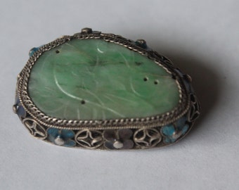 May include: A green jade pendant with intricate silver filigree and blue enamel accents. The pendant is oval shaped and has a carved design.