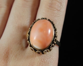 May include: A gold ring with a large oval-shaped coral gemstone set in a twisted wire setting.