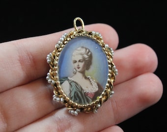 May include: A gold pendant with a blue and white cameo featuring a woman with a white lace collar and a green dress. The pendant is surrounded by a gold rope chain with white pearl accents.