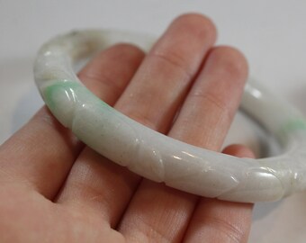 May include: A white jade bangle with green swirls and a carved design. The bangle is smooth and polished.