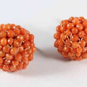 May include: A pair of orange coral earrings, each made of a cluster of small, round beads.