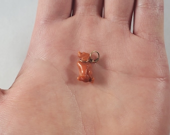 May include: A small, orange coral charm in the shape of a dog, with a gold-colored metal loop.