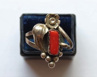 May include: A silver ring with a red coral stone and a floral design. The ring is set in a blue velvet box.