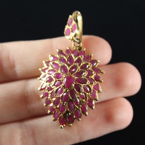 May include: A gold pendant with a teardrop-shaped design featuring a cluster of ruby red gemstones.