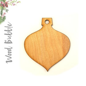 May include: A natural wood ornament shaped like a teardrop with a hole at the top for hanging. The ornament is unfinished and ready to be painted or decorated.