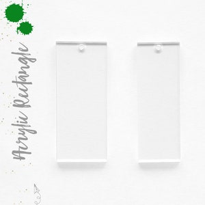 May include: Two clear acrylic rectangle blanks with a hole at the top for jewelry making or crafting. The text "Acrylic Rectangle" is written in gray script on the left side of the image, with green paint splatters.