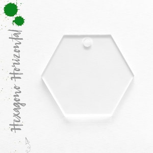 May include: A clear acrylic hexagon ornament with a hole at the top for hanging. The ornament is blank and ready to be decorated.