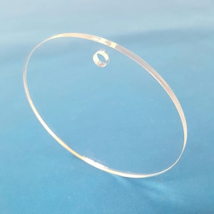 May include: A clear round acrylic blank with a hole in the center. The blank is perfect for crafting and personalization.