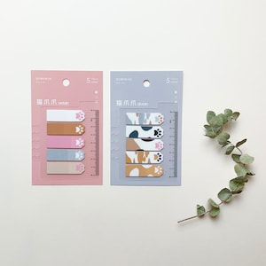 May include: Two packs of colorful cat paw sticky notes. Each pack has five different colors and a ruler on the side. The notes have paw prints on them.