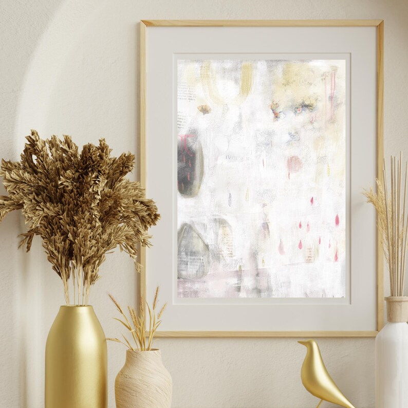 May include: A framed abstract wall art print featuring a white background with subtle grey, gold, and pink accents. The artwork displays soft, layered textures and faint vertical lines, enclosed in a light-colored wooden frame with a white mat border.