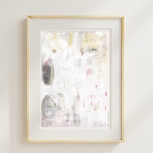 May include: An abstract painting in a light wood frame featuring a white background with soft gray, yellow, and pink accents. The composition includes layered textures, faint vertical lines, and small droplet shapes in pink, with a signature in the bottom right.