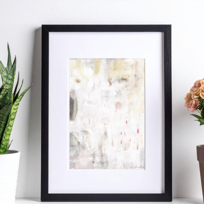 May include: A framed abstract painting featuring a white background with soft beige, grey, and muted pink accents. The artwork includes subtle vertical drips and layered textures within a black frame and a white mat board border.