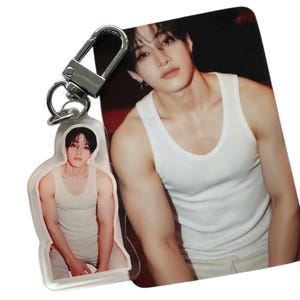 Puede incluir: Un llavero acrílico transparente con una fotografía de una persona con una camiseta sin mangas blanca. El llavero tiene un cierre plateado. Una fotografía más grande de la misma persona con una camiseta sin mangas blanca es visible en el fondo.