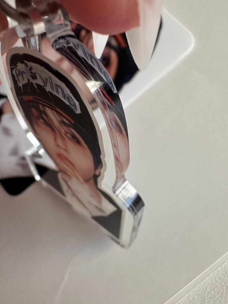 May include: A clear acrylic keychain featuring a printed image of a person with the word "Praying" in a stylized font. The keychain has a silver-colored metal ring.