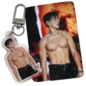 May include: A clear acrylic keychain and a photo card featuring a shirtless person wearing black pants and sunglasses. The keychain has a silver clasp. The photo card has a red and orange background.