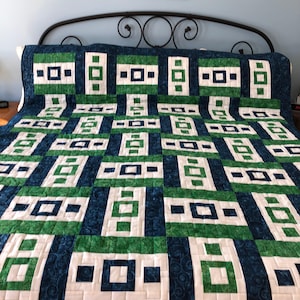 May include: A green and blue quilt with a geometric pattern of squares and rectangles. The quilt is made with a variety of fabrics, including a white fabric with a swirl pattern.