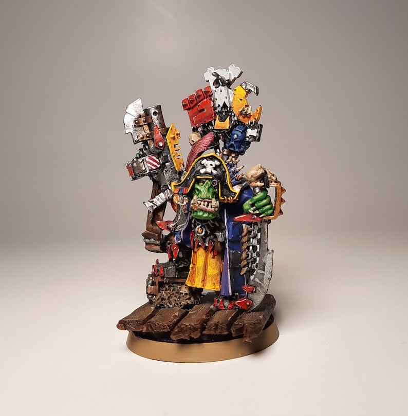 May include: A painted miniature of an Ork warboss, a large green humanoid with a blue and yellow robe, holding a large axe and standing on a wooden base.
