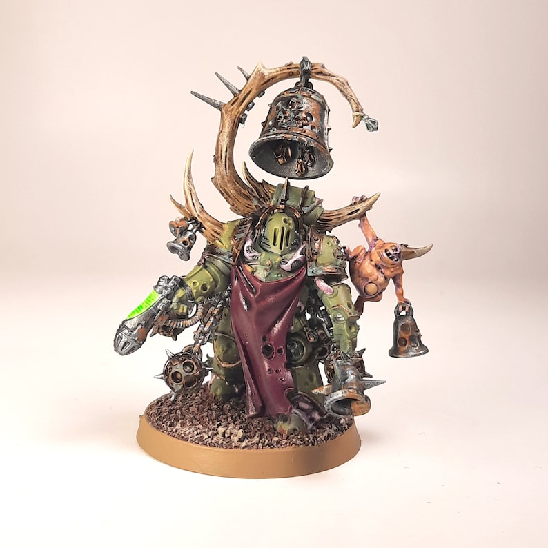 May include: A green and brown painted miniature figure of a Chaos Space Marine with a large bell on a branch, a smaller bell on a chain, and a small, fleshy, pink creature with a bell on its arm.