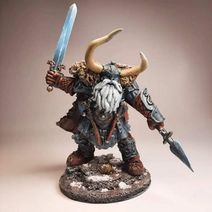 May include: A painted miniature figurine of a dwarf warrior with a horned helmet, a long white beard, and a blue and silver sword. He is wearing a brown leather tunic, blue armour, and a fur cloak. He is standing on a snowy base.