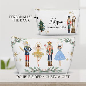 May include: White zippered pouch with a Nutcracker theme. One side features a Christmas tree, the name Alyssa, and the text "Nutcracker 2024". The other side features a mouse, a ballerina, a Nutcracker soldier, and another ballerina. The pouch is double-sided and has a custom gift design.
