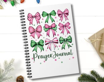Può includere: Un diario bianco a spirale con le parole "Prayer Journal" stampate in verde. La copertina è decorata con fiocchi rosa e verdi con pois bianchi.